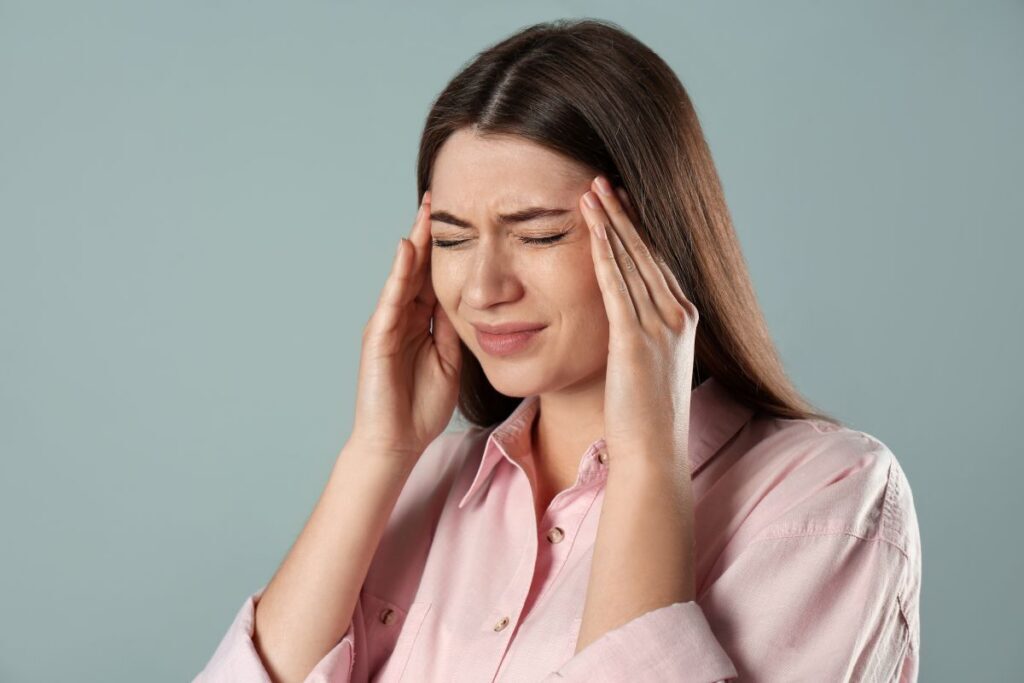 Woman in a pink shirt closes her eyes and presses her temples, signaling a headache or stress relief.
